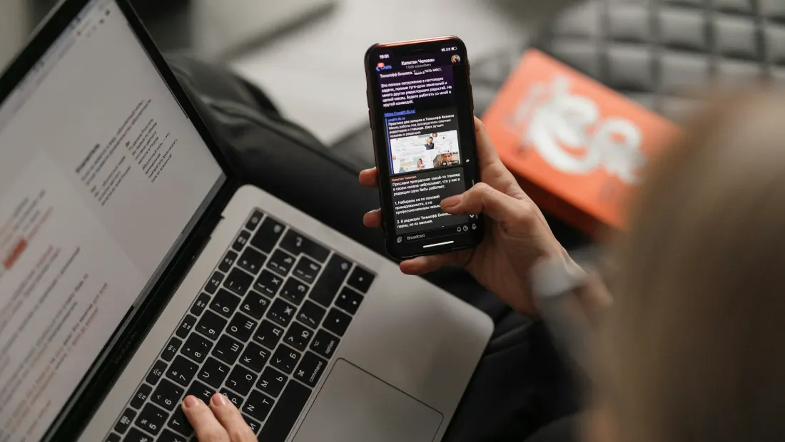 Person reading an email on a smartphone beside a laptop